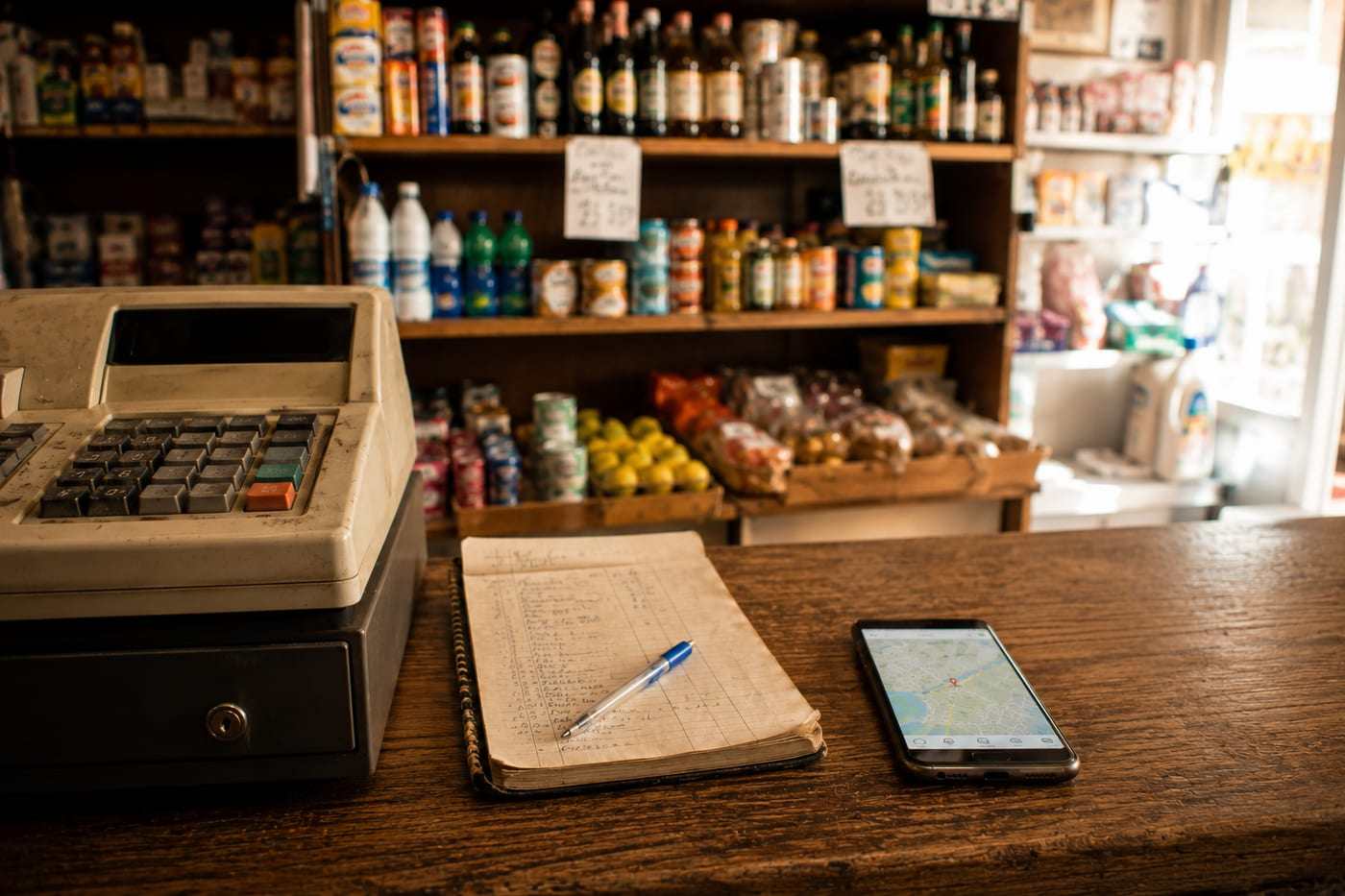 Mostrador de una tienda de barrio con una agenda de pedidos en papel y un móvil con un mapa